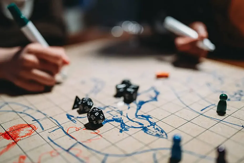 Detalhe focado em dados poliédricos pretos espalhados sobre um mapa de RPG desenhado à mão, com pessoas segurando marcadores em segundo plano.